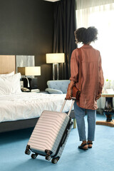 Full length back view of young Black woman suitcase arriving at resort and entering hotel room with...