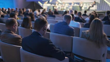 Focused audience at a business conference watching and listening to expert panelists on stage discussing industry trends and insights.