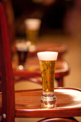 The warmlit pub features tall glasses of frothy beer on wooden bar stools, creating a cozy ambiance
