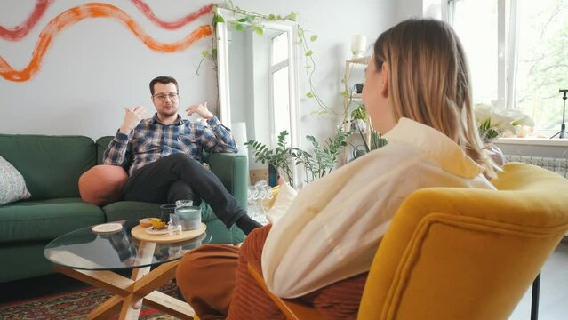 Happy man sitting on sofa and speaking with female psychologist during therapy session