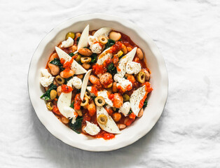 Cooking delicious snack, appetizer, tapas - baked beans with spinach and mozzarella on a light background, top view