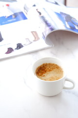 白いテーブルで、エスプレッソと牛乳を混ぜたカフェ・ラッテを飲みながら、雑誌を読んでいるイメージ
