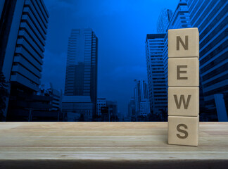 NEWS letter on wood block cubes on wooden table over modern office city tower and skyscraper,...