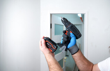 Construction worker holding electric cordless screwdriver in hand at construction site. Accessories for assembling, install furniture, repair home. Home renovation, electric tool for job. Crop view.