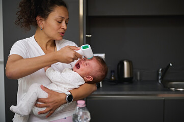 Mother measuring the body temperature of her baby, using contactless electronic digital infrared thermometer. Childcare. Health check