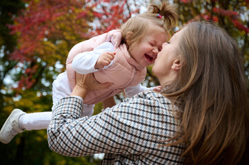 Fototapeta premium Mother and cute baby girl walking in autumn park with leaves on the ground. Mom spending time with a small child in the park. ?oncept of a good mother-child relationship.