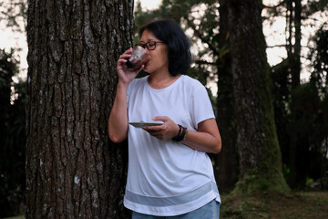 A woman was leaning against a tree trunk while drinking a cup of chocolate