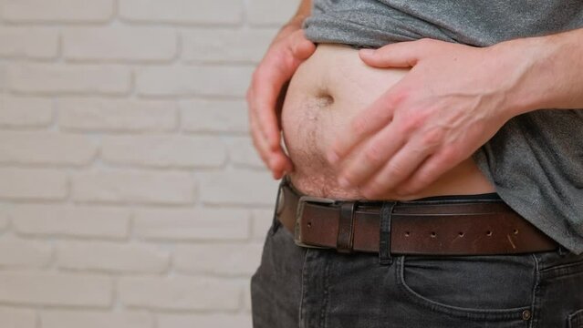 A closeup view of a mans midsection as he pinches his belly fat, indicating issues with weight gain and body image