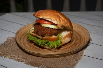 Classic Beef burger with tomato, lettuce and cucumber served in dish isolated on napkin bangladeshi food side view on table