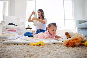 Mom, baby and folding clothes with toys for tummy time or playing on living room floor, carpet or...