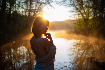 A young attractive woman enjoy sunrise on the water in beautiful nature. In healthy body - healthy mind concept.