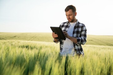 Digital tablet in hands. Handsome man is on the agricultural field at daytime