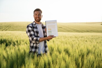 Showing the document with graphs, conception of success. Handsome man is on the agricultural field...