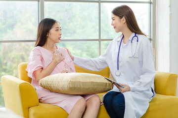 Obraz premium Asian young woman doctor smiling caring supporting touching mature shoulder of female patient sitting on sofa at clinic or hospital. Medicine, healthcare and help people concept