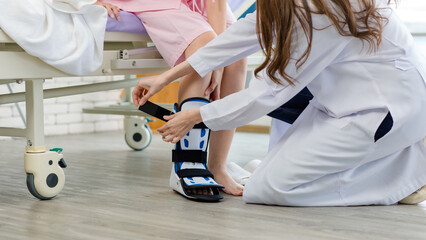 Asian young female physiotherapist fixing walking brace puts a splint on patient leg support injury...