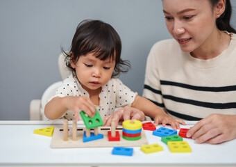 mother teaching her toddler baby girl to playing wooden educational geometric on table