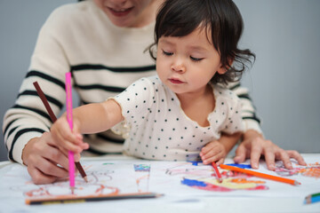 toddler baby training to drawing with colored pencil with mother helping on table