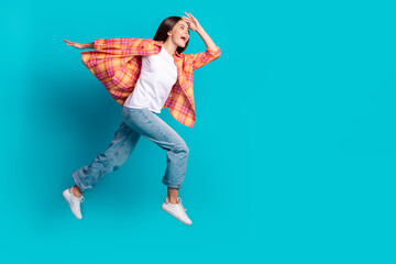 Full size profile photo of nice young girl jump run empty space wear plaid shirt isolated on teal...