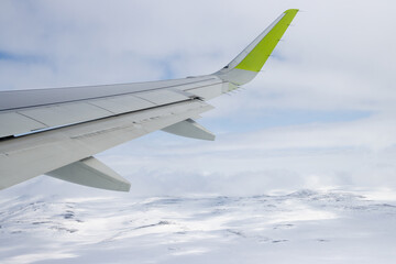 View of an airplane wing and snow-covered hills. Flight over snow-capped mountains. An airliner...