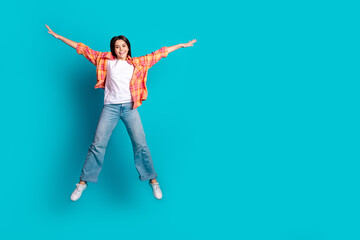 Full size photo of nice young girl jump empty space wear plaid shirt isolated on teal color...