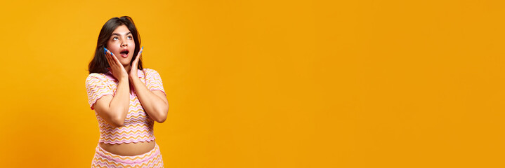 Banner. Emotional young Indian woman posing expressing shock against vibrant yellow studio...