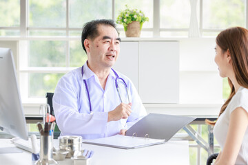 Asian senior man doctor in hospital or clinic talking to nervous young female patient trying to...