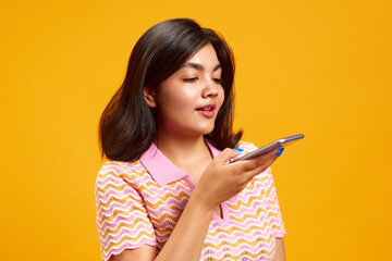 Portrait of you Indian girl talking on smartphone against vibrant yellow studio background....