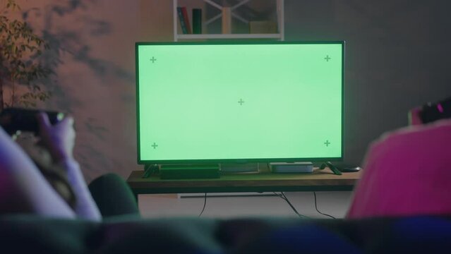 Rear shot of couple friends playing console game tournament. Two players fast clicking their remote controllers during hard game. Boyfriend and girlfriend focused on tv screen videogame