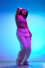 Full length portrait of young brunette Indian girl dancing of joy in motion in pink neon light...