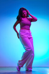 Young Indian woman in stylish attire dancing of joy and happiness in pink neon light against...
