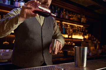 Bartender in uniform pouring drink into shaker behind bar