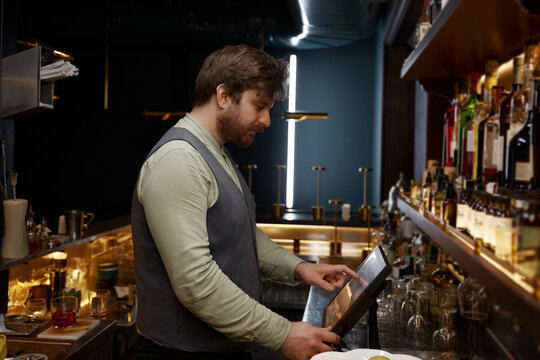 Bartender using digital panel to for processing bar visitors orders - Powered by Adobe