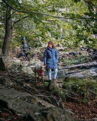 A young woman standing with a Weimaraner in a forest and rural setting. A girl and a Braco de Weimar dog in the forest.