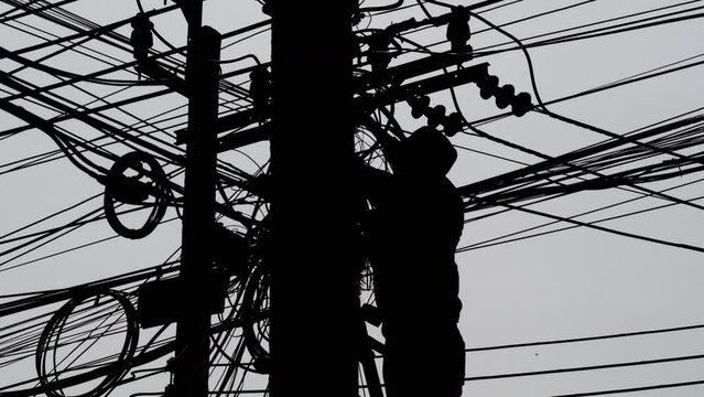 Silhouette of technician in protective gear on a ladder installing optical fiber cables.
