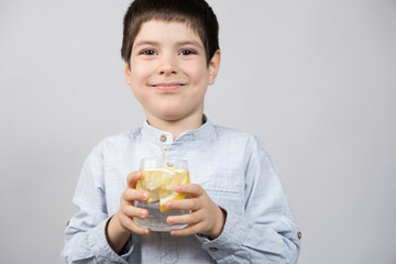 Happy six-year-old boy holding a glass of lemon water in his hands.