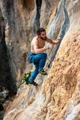 young sporty male climber with long hair climbs a rock.  muscular young man. a man climbs a very difficult route. extreme sport.