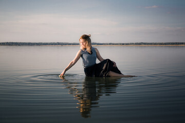 Portrait of beautiful young woman in dress sits in the water doing circles on water. Copy space....
