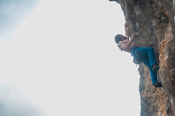 male climber.  strong muscular male rock climber climbs a vertical rock and makes great efforts to...
