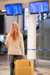 Young woman with luggage checking flight information at airport terminal. Concept of travel,...
