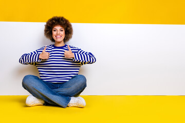 Full length photo of cool woman dressed striped shirt sit near placard empty space show thumbs up...