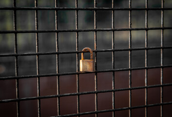 Rusty and aged padlock on a meshed grill from an industrial site representing a romance...