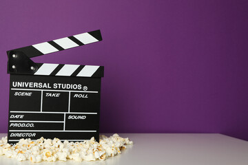 Clapperboard and popcorn on table on purple background, space for text