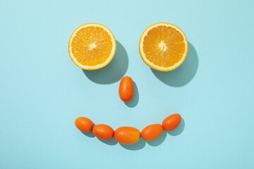 Whole kumquats and two half of orange on blue background, top view