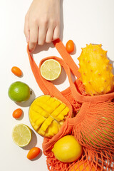 Set of tropical fruit in bag and hand on white background, top view