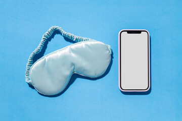 Top view of smartphone and sleeping mask on empty blue background. Concept of health care and rhythm of sleep