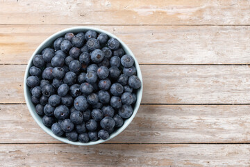 Blueberries in green bowl on wooden table. Top view. Copy space