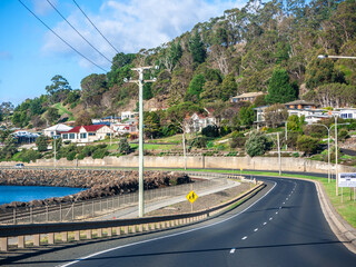 An asphalt road runs along the coastline in Burnie, with residential houses visible in the...