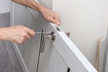 Worker installs a door handle on a door using a screwdriver. Tightening the screws. Home renovation. Door installation. Close-up.