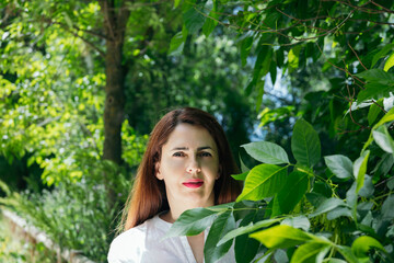 Portrait of a 45 year old mature woman relaxing looking at the camera among green foliage in a park...