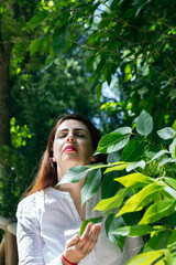 Portrait of a 45 year old woman with her eyes closed relaxing outdoors among the green leaves of a...